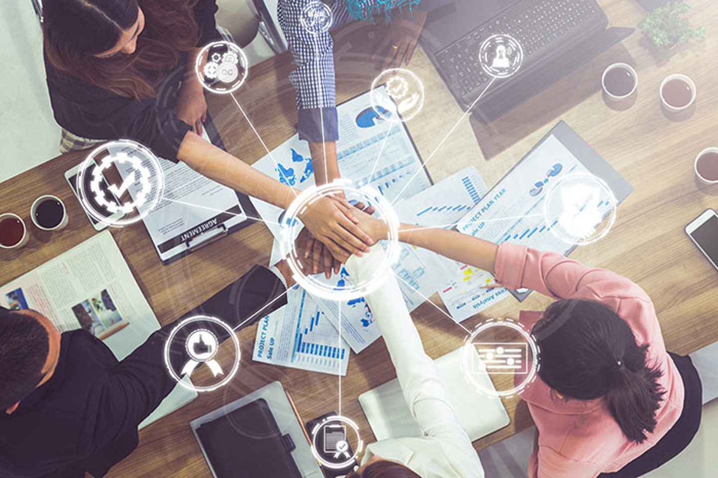 work team sat around desk placing  their hands on top of each other with graphics over top showing signs of positivity